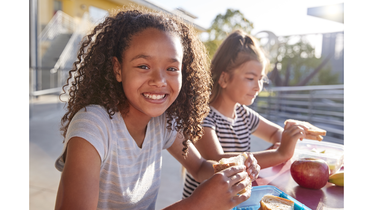 Girlfriends at school lunch table, one smiling to camera