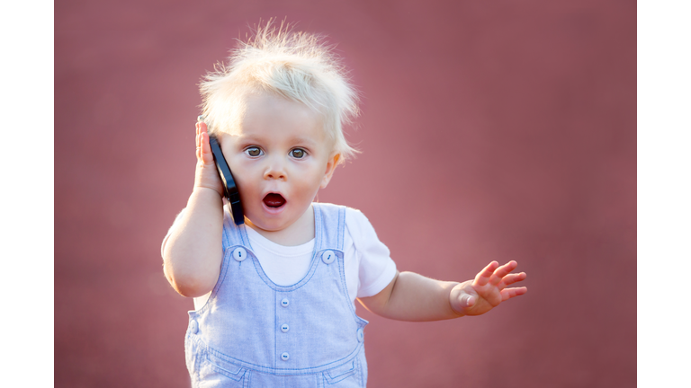 Cute baby boy playing with mobile phone in the park, digital technologies in the hands of a child