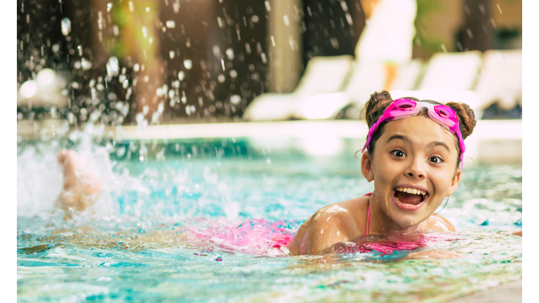 Happy beautiful little smiling girl in goggles and swimsuit in the pool has fun while vacationing or swimming lessons.