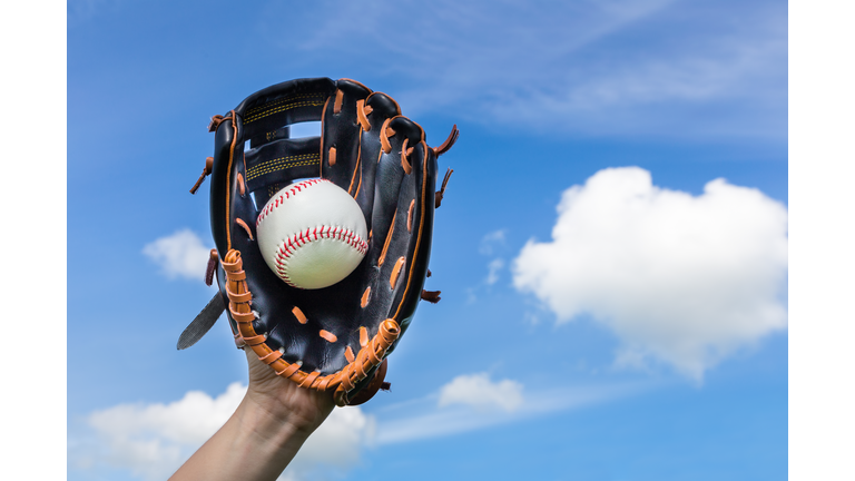 Hand holding baseball in glove with blue sky