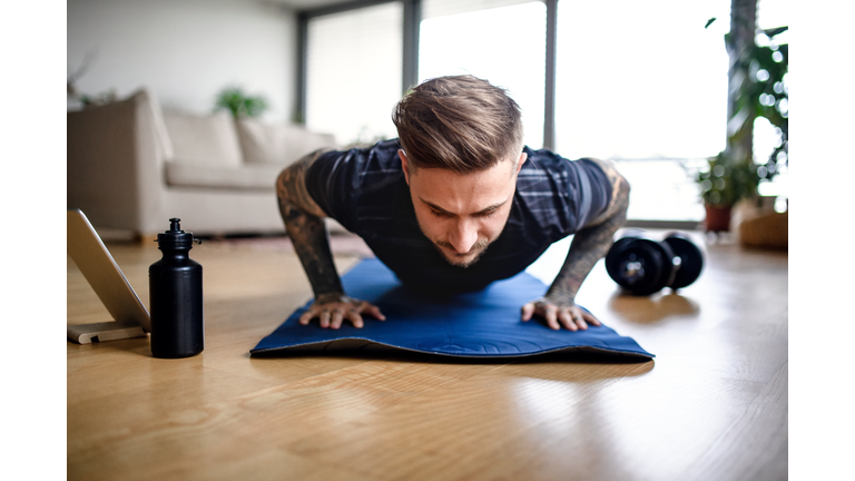 Front view portrait of man with tablet doing workout exercise indoors at home.