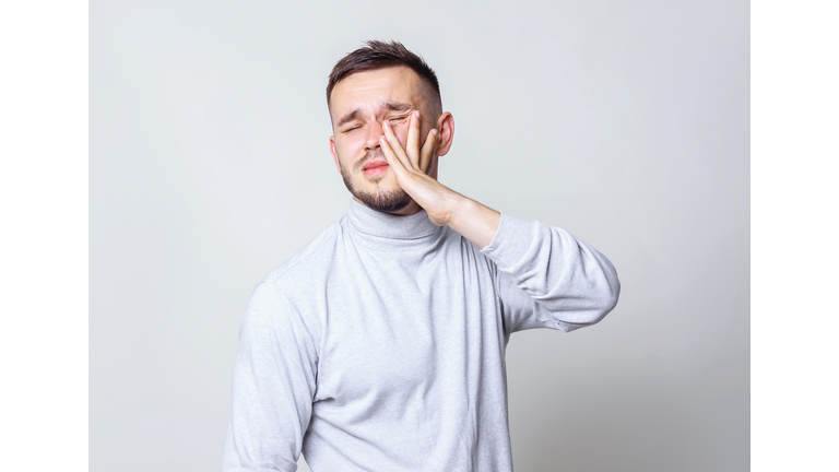 Man hit himself. Man in white turtleneck giving a slap in the face oneself on grey background copy space