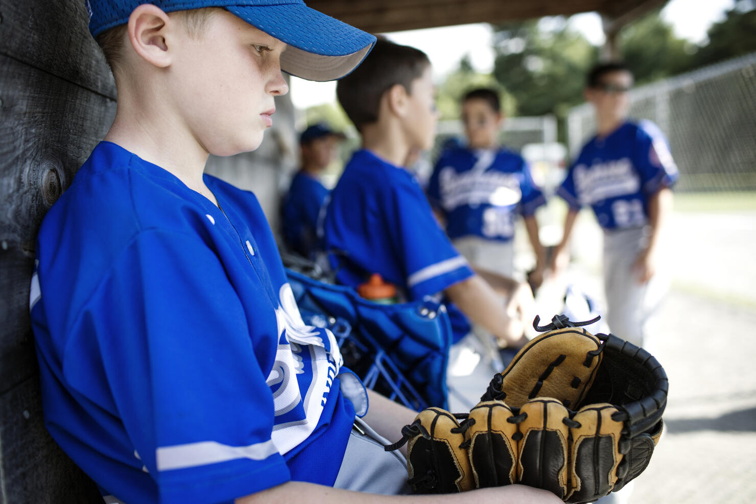 Thoughtful boy with sports glove sitting in dugout