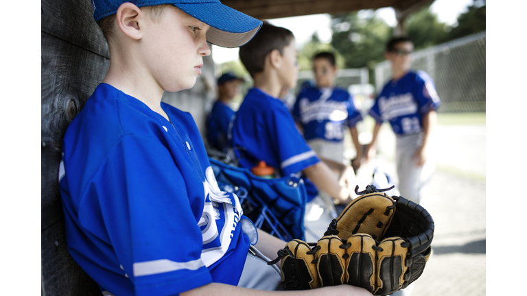 Thoughtful boy with sports glove sitting in dugout