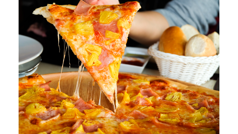 Close up Woman's hand picked Hawaiian pizza from a wooden tray on the table.