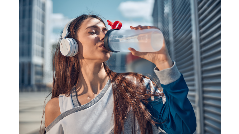 Sportswoman in headphones holding a plastic bottle