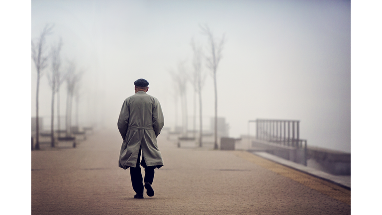 Old man walking down empty foggy road