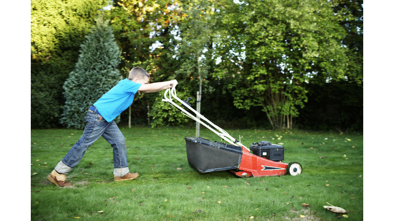 Boy (7-9) pushing lawnmower, side view