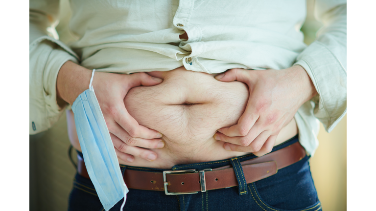 male with medical mask checking body fat by grabbing stomach