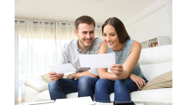 Happy couple looking and checking bills at home