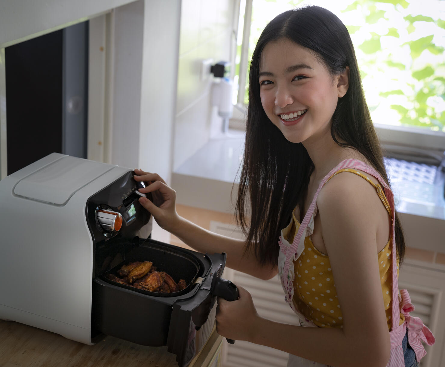 Asian girl cooking a fried chicken by Air Fryer machine in her kitchen at home