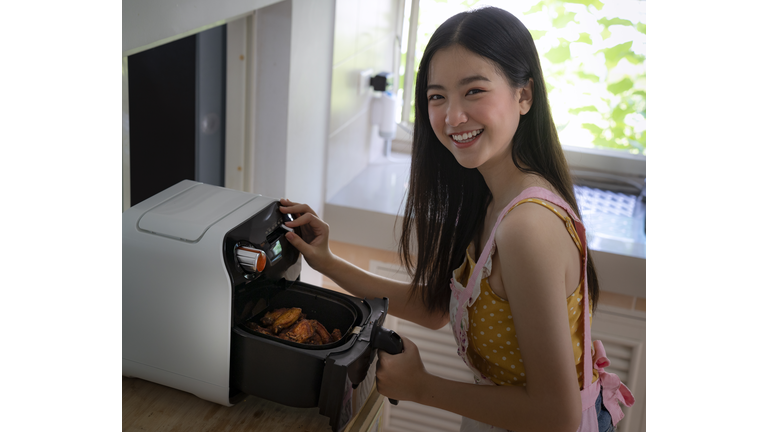 Asian girl cooking a fried chicken by Air Fryer machine in her kitchen at home