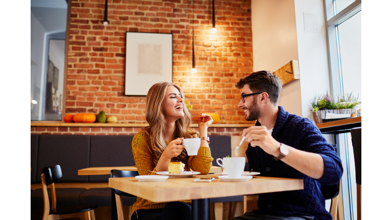 Couple of young people drinking coffee and eating cake in a stylish modern cafeteria