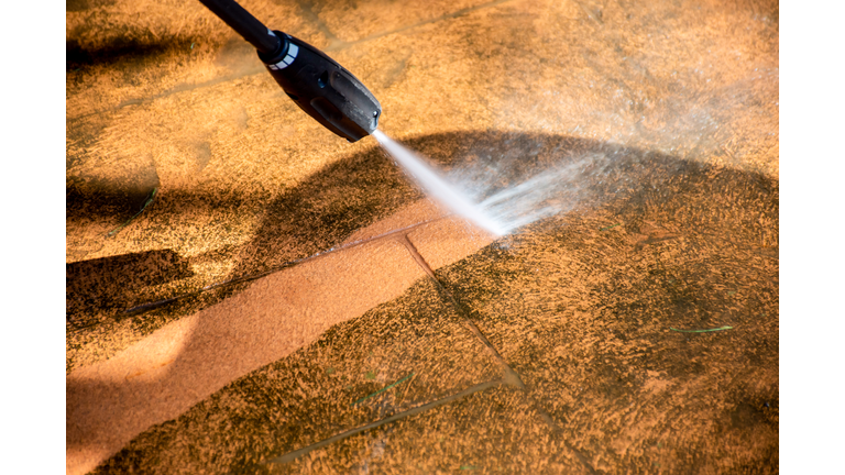 Cleaning backyard paving tiles with pressure washer.