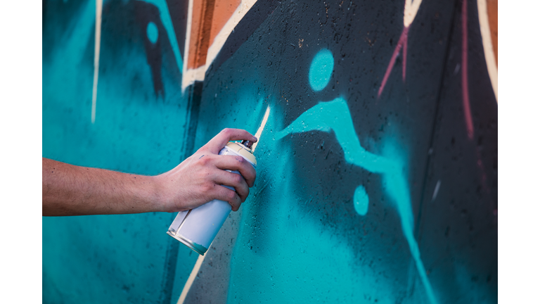 Street artist painting colorful graffiti on generic wall - Modern art concept with urban guy performing and preparing live murales with multi color aerosol spray