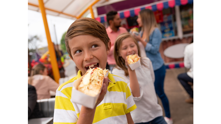Happy kids eating junk food at an amusement park