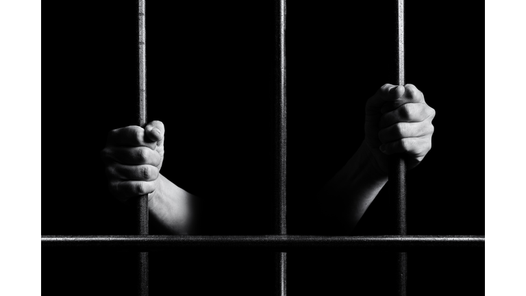 Conceptual monochrome photo of hands holding the bars of a prison door