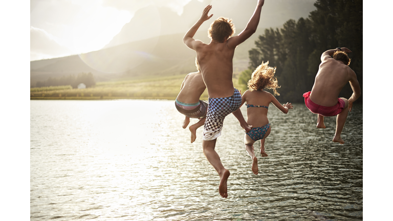 four friends jumping into a lake in the mountains