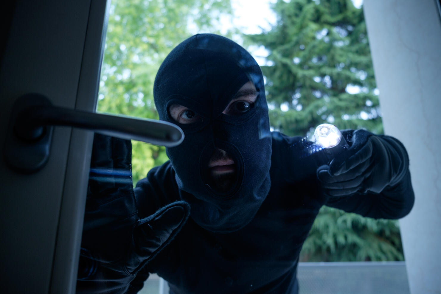 Burglar wearing a balaclava looking through the house window