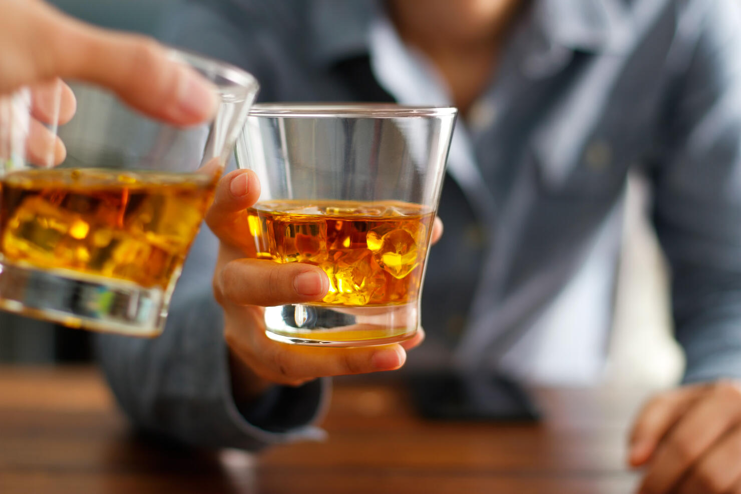 Close-up two men clinking glasses of whiskey drink alcohol beverage together at counter in the pub