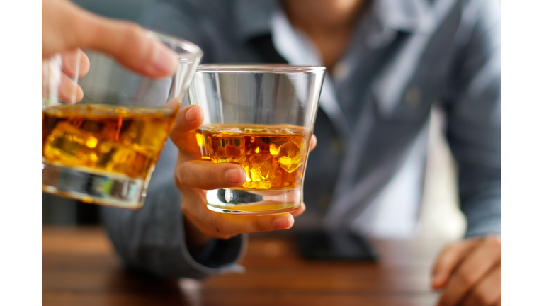 Close-up two men clinking glasses of whiskey drink alcohol beverage together at counter in the pub