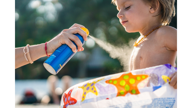 Little boy getting sun protection from his parent on the beach.