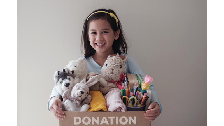 Mixed Asian young volunteer girl holding a box full of used toys, cloths, books and stationery for donation