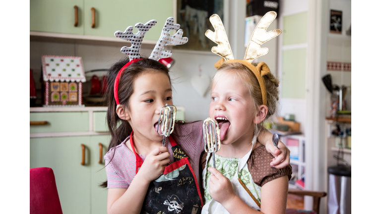 Girls tasting mix from egg beater whilst preparing food for Christmas