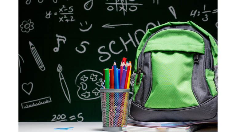 Education concept - green backpack, notebooks and school supplies on the background of the blackboard
