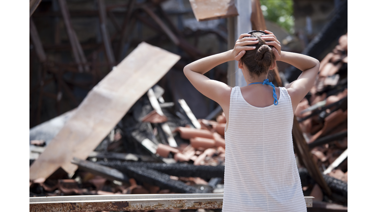 woman stands in front of burned out house