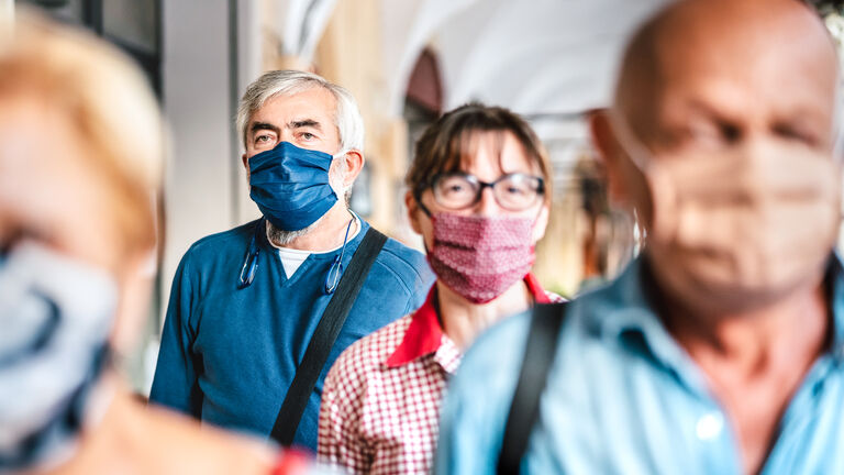 Crowd of adult citizens walking on city street - New reality lifestyle concept with senior people with covered faces - Selective focus on bearded man with blue protective mask