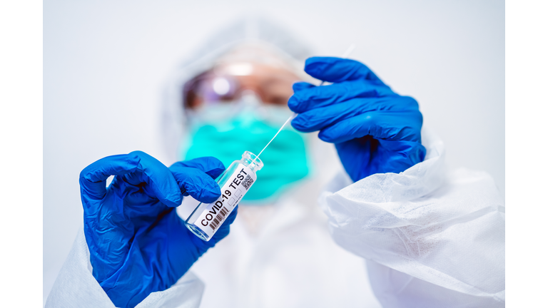 Doctor in protective gloves & workwear holding open test tube and taking out sampling swab for novel Covid-19 test