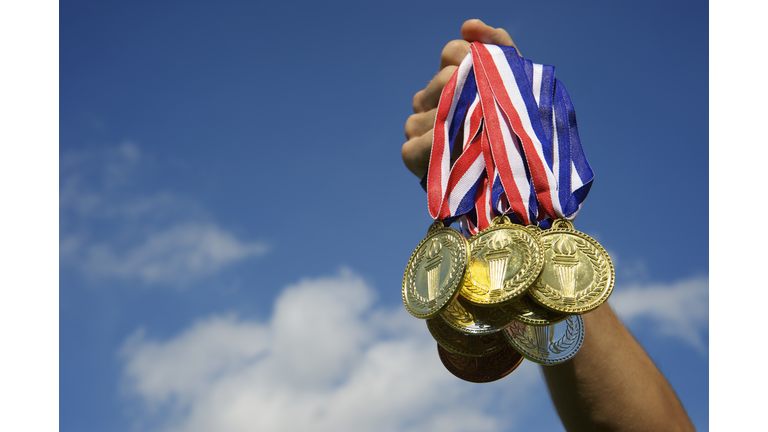 Athlete Hand Holding Up Bunch of Gold Medals Blue Sky