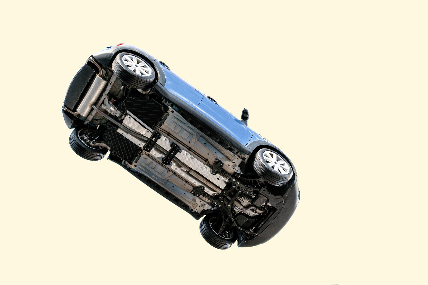 A car flying through the air (in the pale blue sky) with the underside including, wheels, engine and exhaust pipe visible