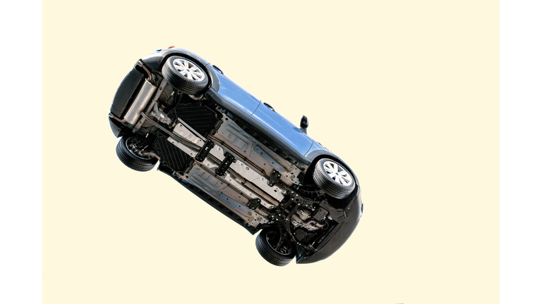 A car flying through the air (in the pale blue sky) with the underside including, wheels, engine and exhaust pipe visible