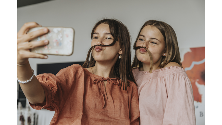 Friends making fake mustache with hair while taking selfie at home