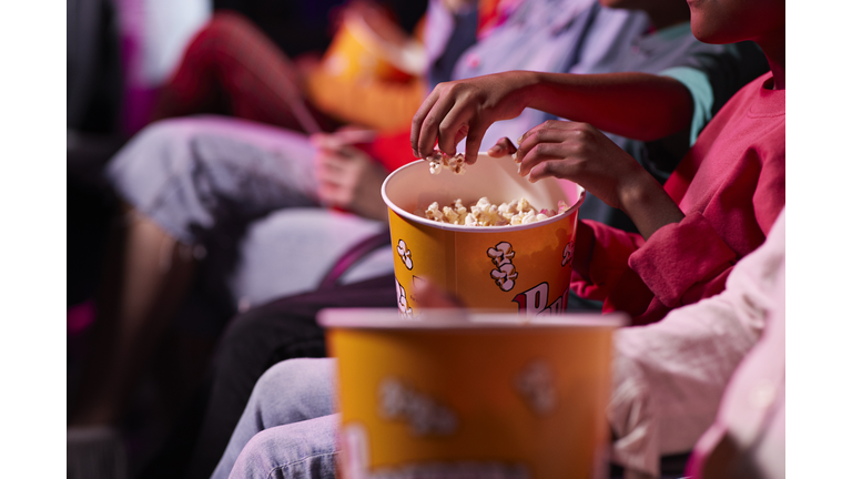 Midsection of friends sharing popcorn while sitting in theater