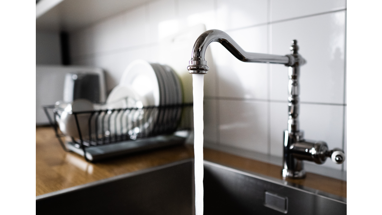 Water flowing out of a kitchen stainless steel tap into the sink. Wasting water by leaving a chrome faucet tap running. Water misuse in domestic duties and activities. Overusing household water.