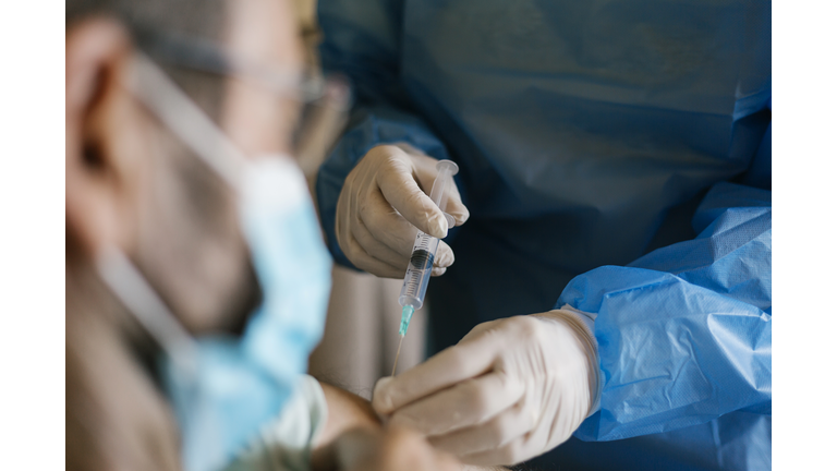 Doctor injecting covid-19 vaccine to senior man at his home.