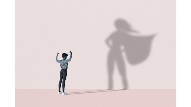 Woman flexing muscles in front of superhero shadow