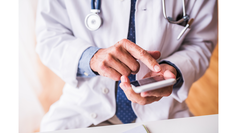 Senior doctor with smartphone working at the office.