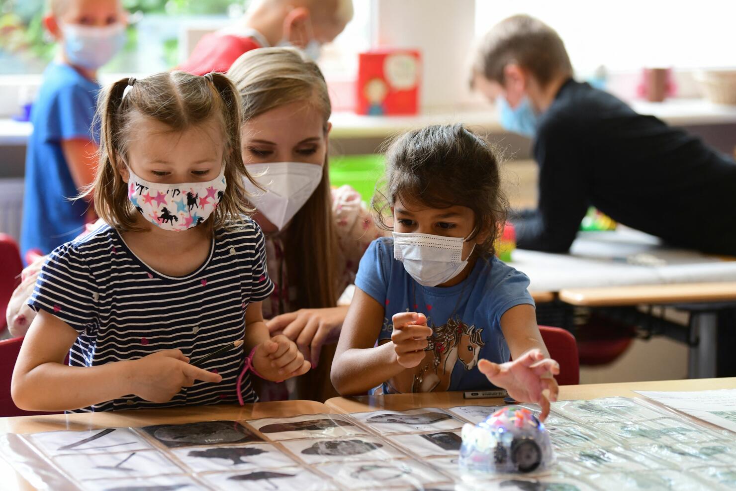 Two young students and teacher wear masks