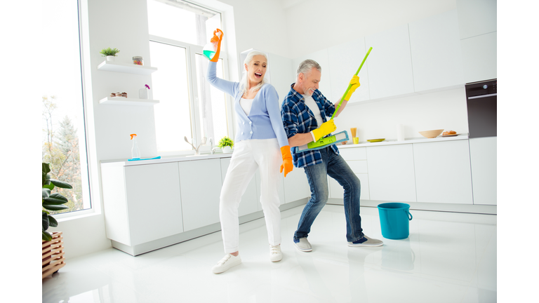 Full size, fullbody portrait of crazy foolish funny mad cool couple of senior dancing, singing, man playing on mop like guitar, woman holding spray in raised hand, positive people concept