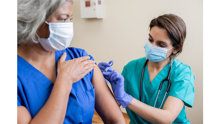 Nurse gives senior adult healthcare worker the Covid-19 vaccine