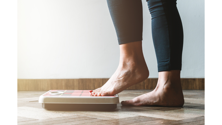 Female checking kilogrammes getting on the scale - self care and body positivity concept - warm flare on left