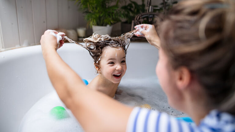 Mother with small daughter in bathroom at home, having fun in bath.