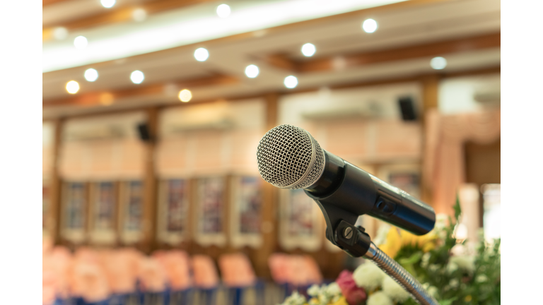 Microphones on abstract blurred of speech in seminar room or front speaking conference hall light, color chairs for people in event meeting convention hall in hotel. Vintage tone