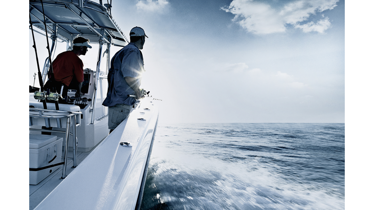 "Monochromatic shot of two men driving and fishing from speedboat, Miami, USA"