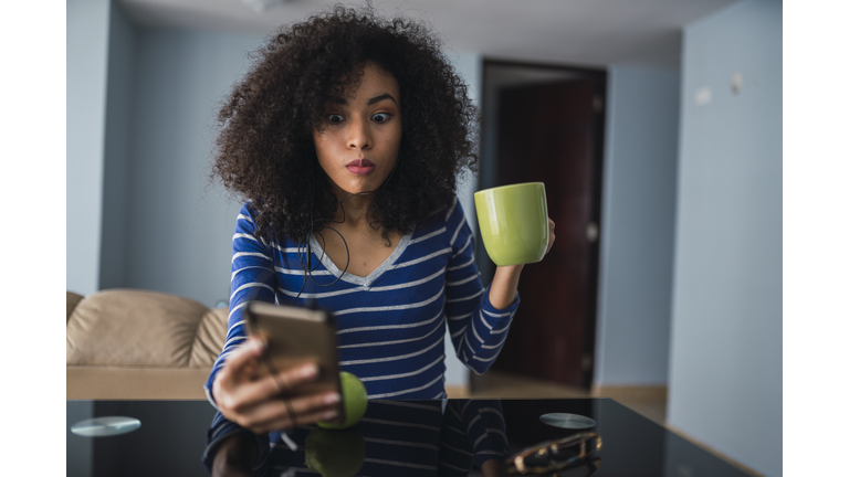 Portrait of young woman with mug starring at cell phone