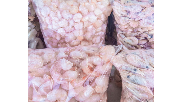 Transparent plastic bag with large king prawns, frozen seafood on the counter of the fish market, wholesale, background of frozen food with snow and frost